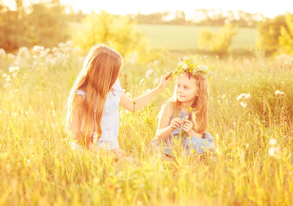 Two little sisters weave wreaths of flowers — Stock Photo, Image