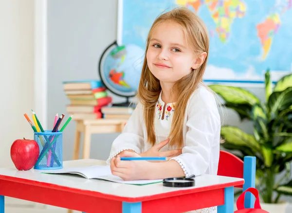 Piccola ragazza bionda sedersi alla scrivania bianca e ridere in classe della scuola — Foto Stock