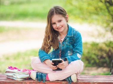 Küçük kız parkta telefonuyla oturuyor