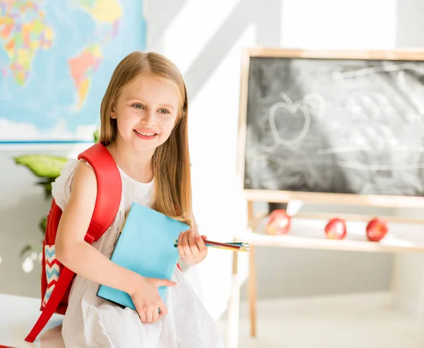 Pequeña rubia sonriente de pie en el aula de la escuela — Foto de Stock