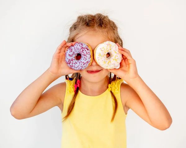 Feliz linda chica rubia sosteniendo dos donuts en sus ojos —  Fotos de Stock