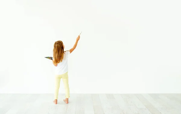 Kleines Mädchen malt an weiße Wand drinnen — Stockfoto