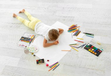 Küçük kız kağıda çiziyor, yerde yatıyor.