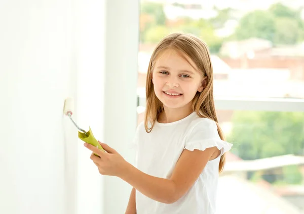 Pequena menina bonito pinta uma parede com rolo de pintura — Fotografia de Stock