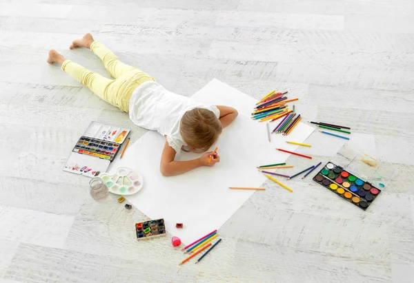 Küçük kız kağıda çiziyor, yerde yatıyor.