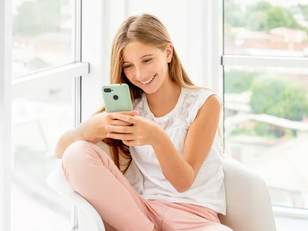 Adolescente menina passar o lazer com seu telefone dentro de casa — Fotografia de Stock