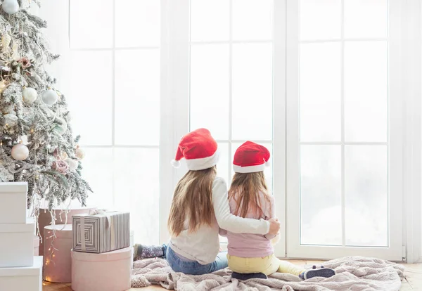 Hermanas se sientan abrazándose cerca del árbol de Navidad —  Fotos de Stock