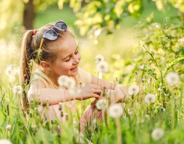 Kleines Mädchen sitzt auf Löwenzahnfeld — Stockfoto