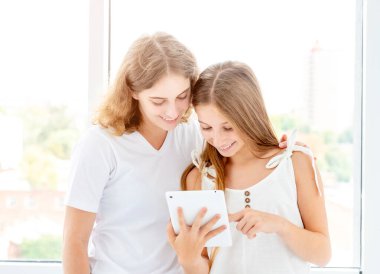 Pencerenin yanında duran tablete bakan kızlar