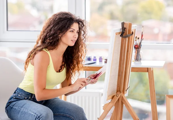 Smiling artist painting on easel — Stok Foto