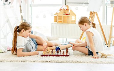 Güzel kız kardeşler yerde satranç oynuyor.