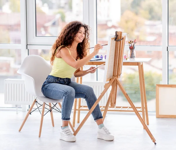 Smiling artist painting on easel — Stok Foto