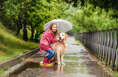 Küçük kız şemsiyesini köpekle paylaşıyor