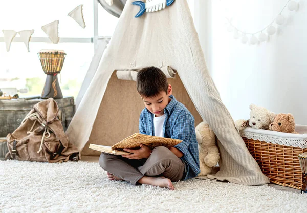 Little boy reading paper book in room