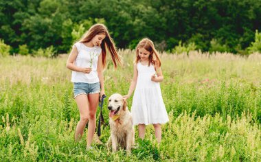 Çiçekli çayırda köpekli kız kardeşler