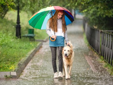 Genç kız köpekle yağmurun altında yürüyor.