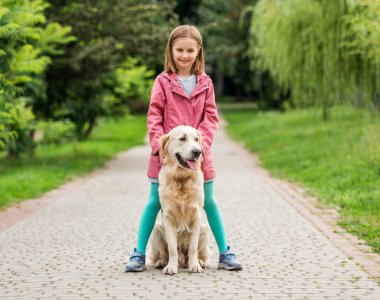 Ayaklarının arasında köpekle duran küçük kız.