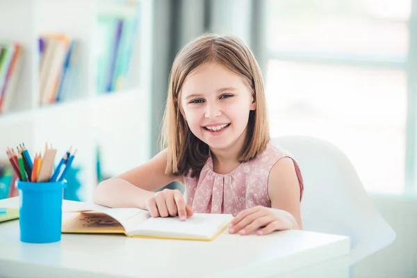 Schoolgirl with textbook sitting at desk — Stock Photo, Image