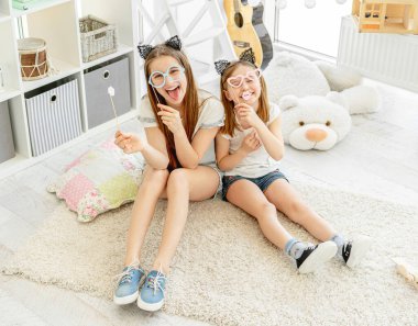 Bardakları tutan kız kardeşler ve çubuklarda dudaklar.