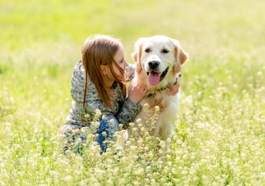 Gülümseyen küçük kız sevimli köpeğe bakıyor.