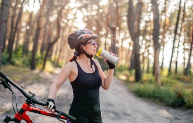 Ormanda su içen bisikletli kadın.