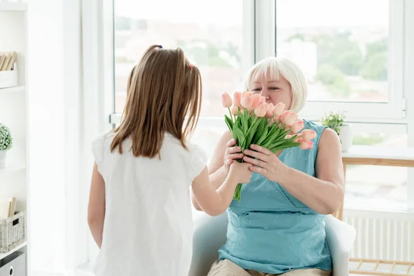 Niña dando flores a la mujer mayor — Foto de Stock