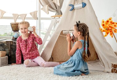 Küçük kız kardeşler ev yapımı telefonlarla oynuyorlar.