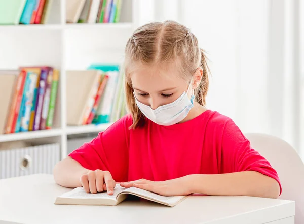 Schulmädchen in Schutzmaske liest Buch — Stockfoto