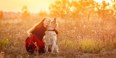 Mutlu genç kız sahada köpeğe sarılıyor.