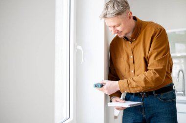 Mutlu Adam, pencerenin açılışını özel bir cihazla ölçüyor ve ölçümleri kaydediyor.