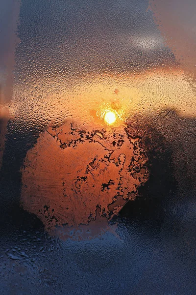 Eismuster, Wassertropfen und Sonnenlicht auf einem Fensterglas im Winter — Stockfoto