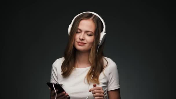 Hermosa mujer caucásica con auriculares bailando y sonriendo a la cámara . — Vídeo de stock