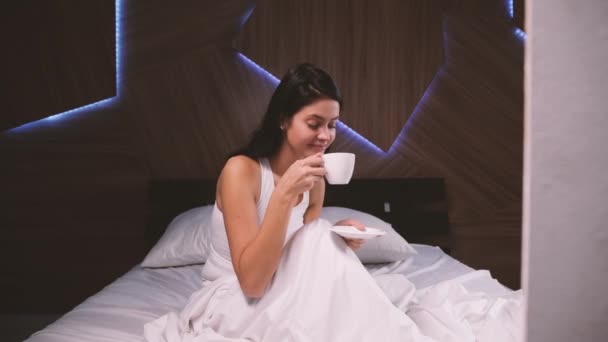 Aantrekkelijke jonge meisje thuis. Koffie drinken in haar bed — Stockvideo