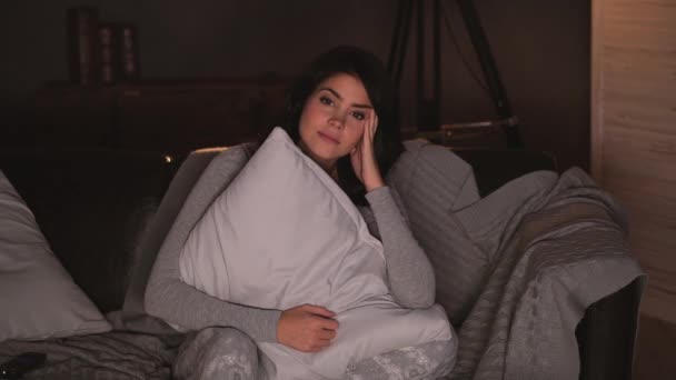 Vacker kvinna tittar på en skräckfilm på tv medan du sitter på soffan hemma — Stockvideo
