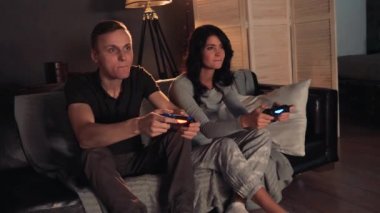 Konsolda video oyunu oynarken bir çift. Evde koltukta oturuyor. Erkekler kazanır.