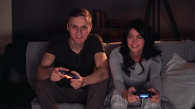 Konsolda video oyunu oynarken bir çift. Evde koltukta oturuyor. Erkekler kazanır.