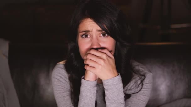 Mujer bonita viendo algunas noticias terribles en la televisión mientras está sentado en el sofá en casa — Vídeos de Stock