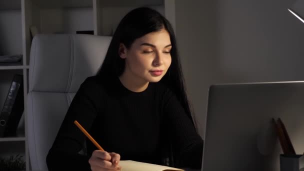 Businesswoman in office. Writing in notebook and looking at camera. Evening. — Stock Video