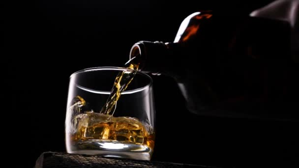Whiskey in het glas uit de fles te gieten. Met ijsblokjes. — Stockvideo
