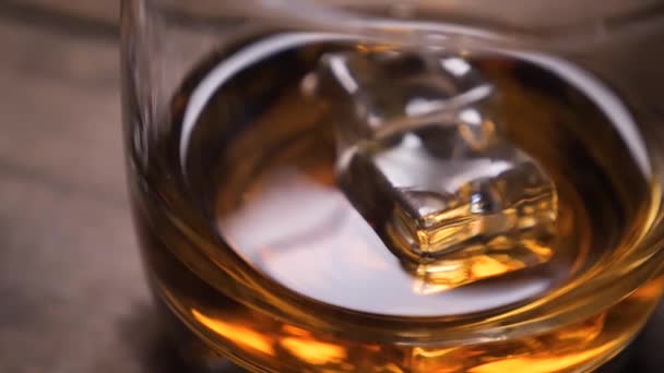 Whiskey pouring in the glass from the bottle. With ice cubes. — Stock Video