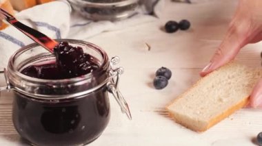 Tanınmayan kişi ekmeğe reçel sürüyor.