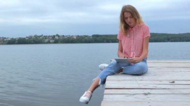Tablet pc ağır çekimde lake yakınındaki otururken swiping sarışın saçlı güzel beyaz kadın