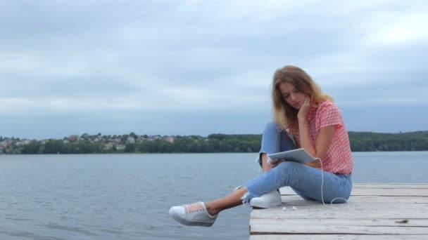 美丽的年轻女性观看在平板电脑 而坐在附近的湖泊慢动作 — 图库视频影像