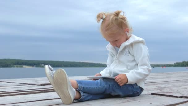 Pretty Little Girl Watching Tablet While Sitting Lake Slow Motion — Stock Video