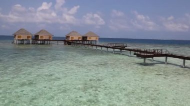 Su Villaları (Bungalovlar) ve yaz günü Maldivler 'deki tropik sahildeki ahşap köprü 