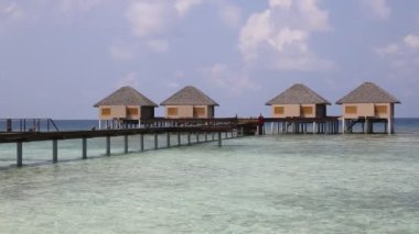 Su Villaları (Bungalovlar) ve yaz günü Maldivler 'deki tropik sahildeki ahşap köprü 