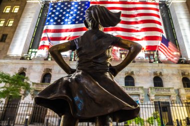 NEW YORK CITY, USA - MARCH 15, 2020:  Fearless Girl Statue looking up at  New York Stock Exchange building at Wall Street in Manhattan at night, New York City, USA clipart