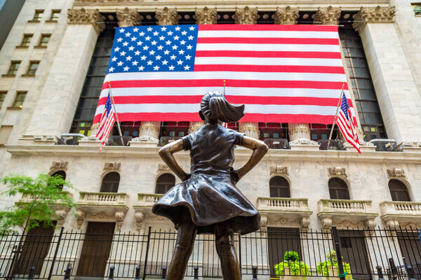 NEW YORK CITY, USA - MARCH 15, 2020:  Fearless Girl Statue looking up at  New York Stock Exchange building at Wall Street in Manhattan, New York City, USA