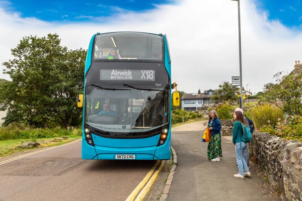 NORTHUMBERLAND, İngiltere - 15 Ağustos 2025: Bir otobüs durağında bekleyen yolcular Craster Köyü, Northumberland, İngiltere 'deki Arriva X18 halk çift katlı otobüs için