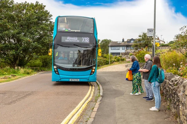 NORTHUMBERLAND, İngiltere - 15 Ağustos 2025: Bir otobüs durağında bekleyen yolcular Craster Köyü, Northumberland, İngiltere 'deki Arriva X18 halk çift katlı otobüs için